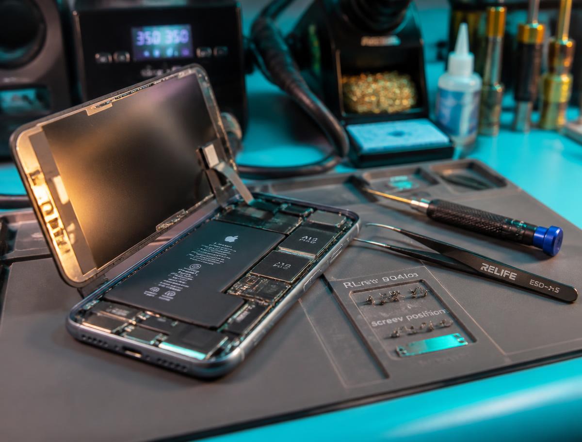 A technician's workbench with a disassembled smartphone and precision repair tools